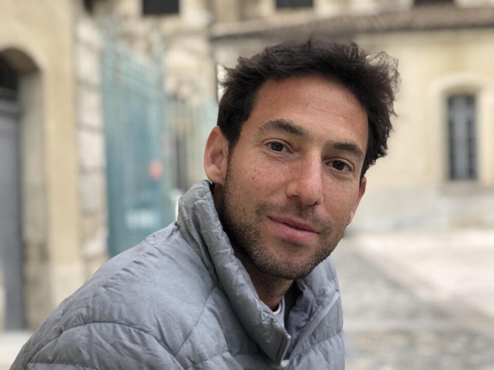 On voit M. Herrmann qui sourit à la caméra. En arrière-plan, les rues de Valence.