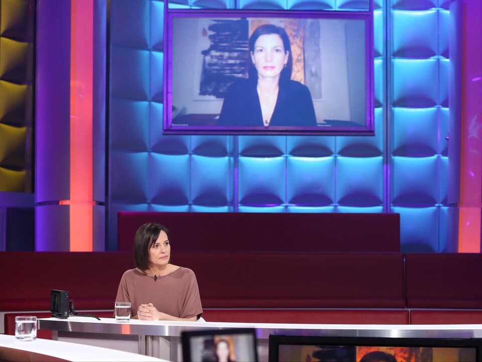 Isabelle Charest est assise dans le studio et Geneviève Guilbault  apparaît sur un écran suspendu derrière elle. 