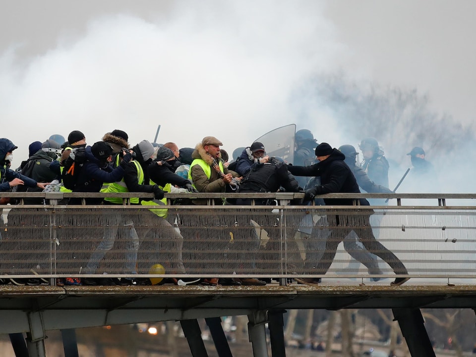 Un homme en noir s'en prend à un policier vêtu d'une tenue antiémeute lors d'affrontements à Paris, en France.