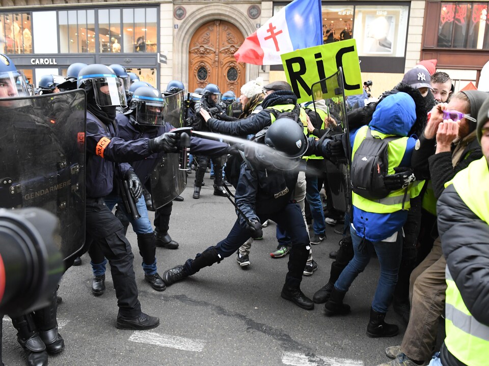 Un policier asperge des manifestants de poivre de cayenne alors qu'un autre les repousse avec un bouclier antiémeute dans une rue de Paris.