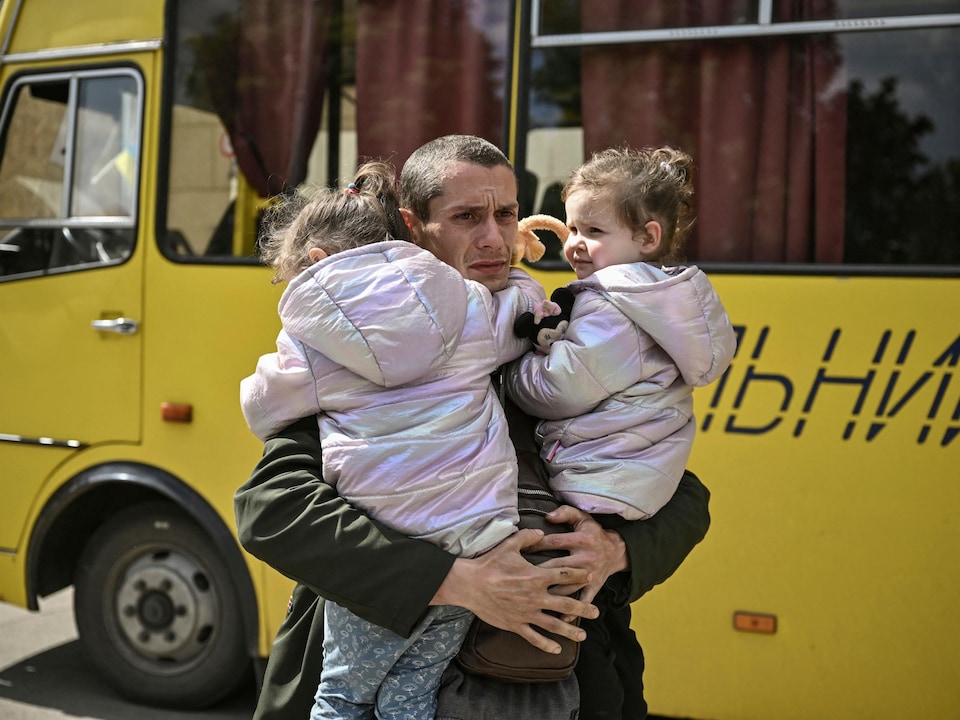 A Ukrainian father holds his twin daughter in his arms in front of a bus