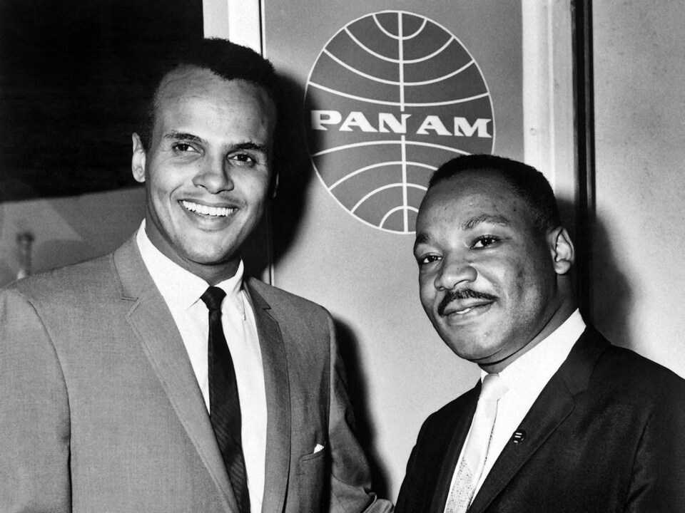 On voit les deux hommes sourire à la caméra. Photo en noir et blanc.