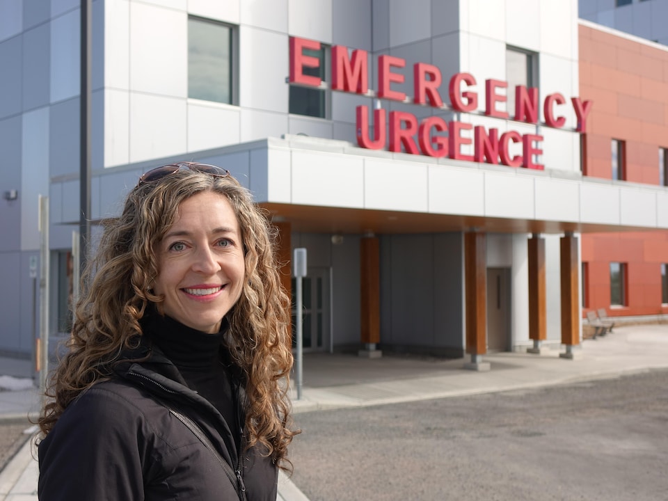 On voit Mme Howard qui sourit à la caméra, devant l'entrée de l'urgence de l'hôpital territorial Stanton.