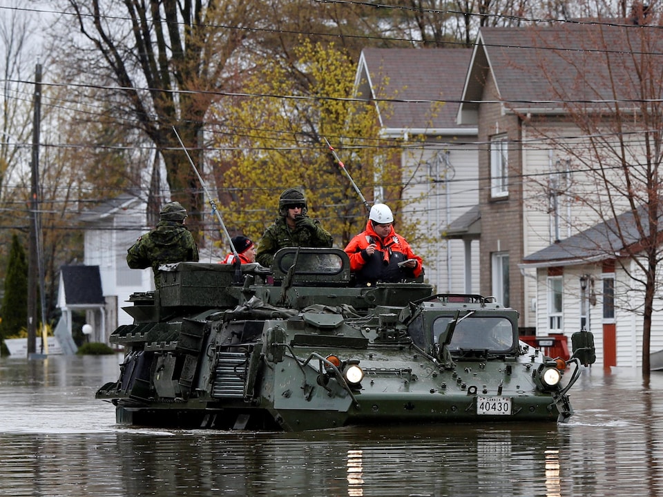 Des soldats canadiens sur un véhicule blindé dans une rue inondée.