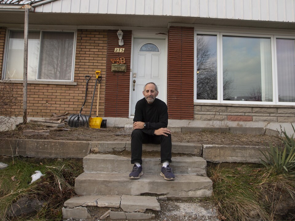 Un homme assis sur les marches devant un bungalow.