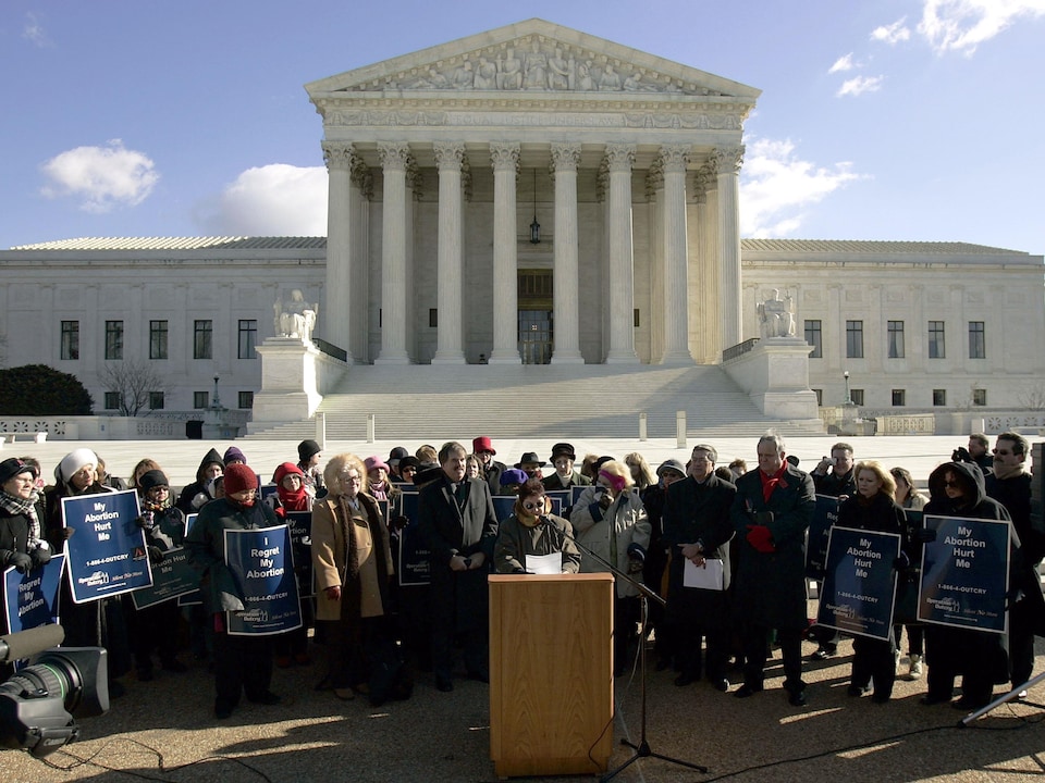 Entourée de gens avec des pancartes, une femme prononce un discours devant la Cour suprême.