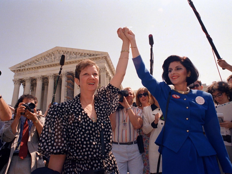 Deux femmes se tiennent la main dans les airs devant l'édifice de la Cour suprême des États-Unis.