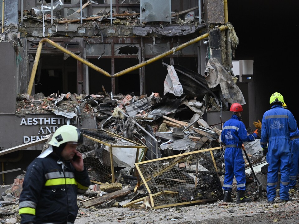 Des sauveteurs ukrainiens devant la façade détruite d'un immeuble. 