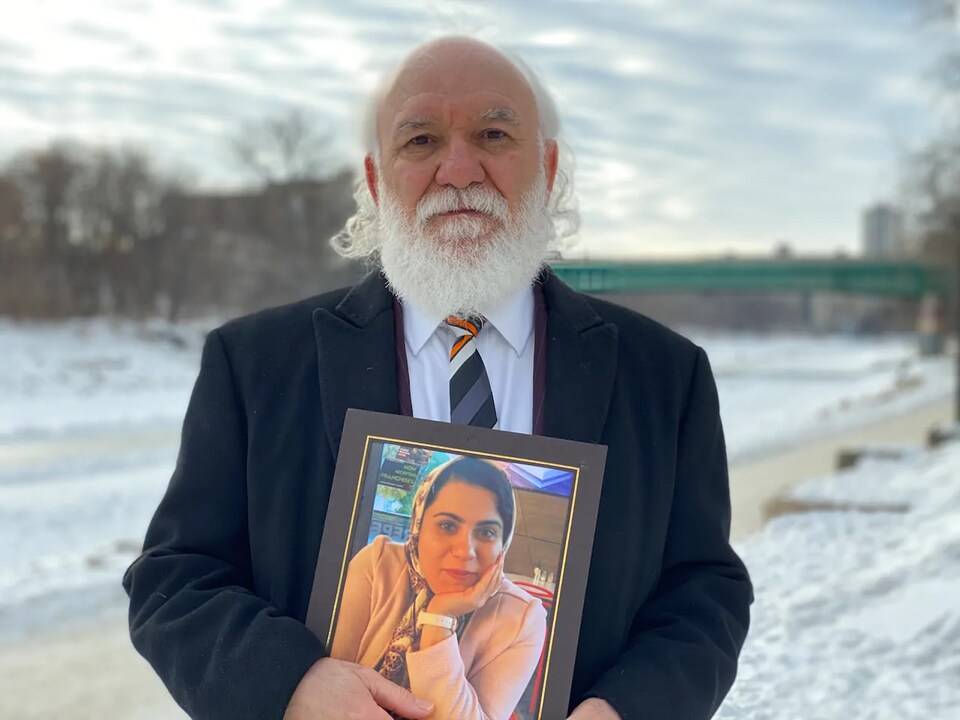 L'homme est dehors près de la rivière gelée et tient un cadre renfermant la photo de sa fiancée.