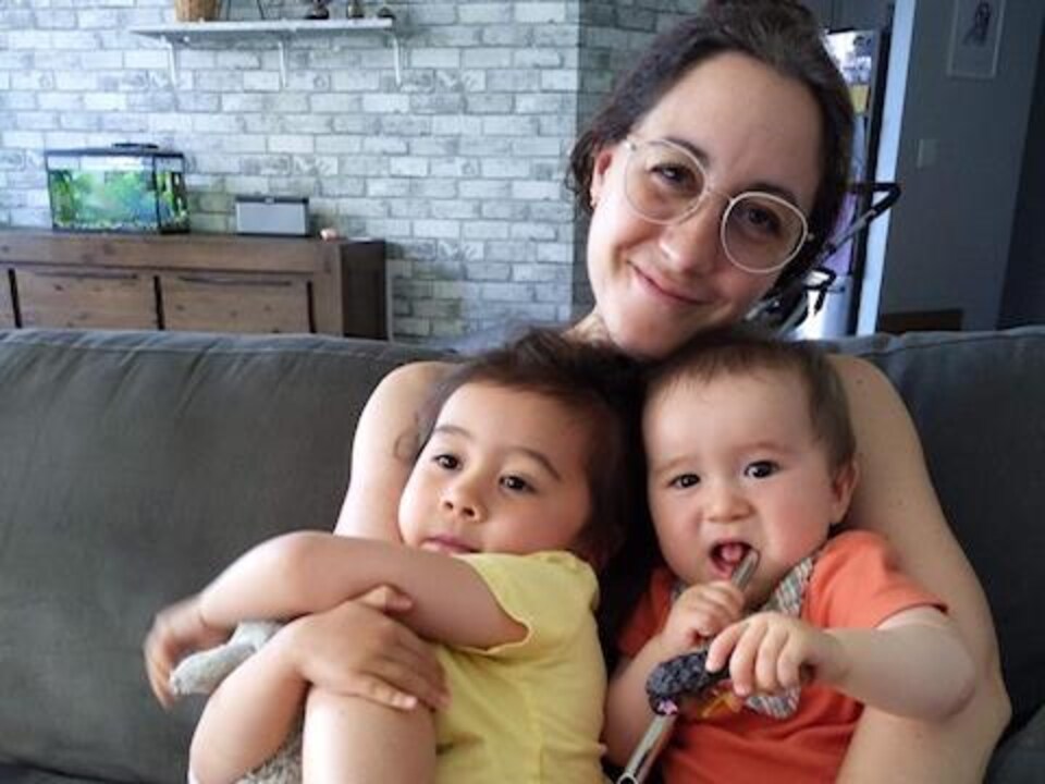 Laura Shinoki, assise sur un canapé, tient ses deux enfants dans ses bras.