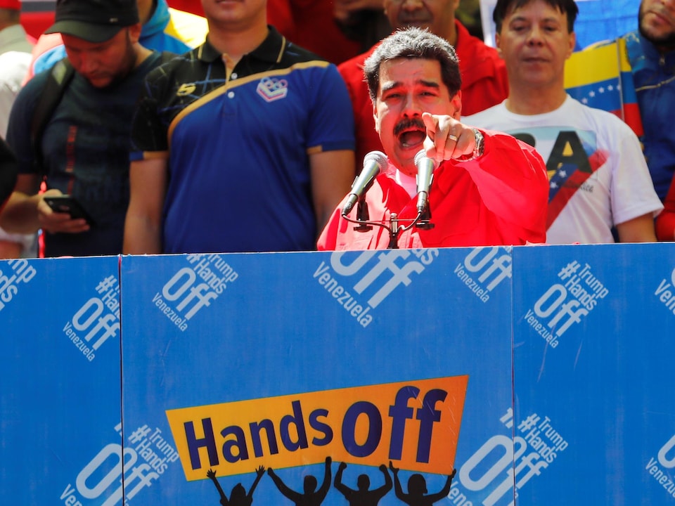 Un homme pointe du doigt dans la direction de la caméra alors qu'il livre un discours derrière deux micros sur une estrade sur laquelle il  est écrit en anglais: « Trump ne touche pas au Venezuela ».