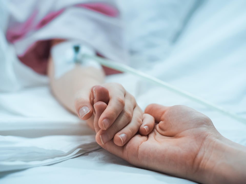 Une personne tient la main d'un malade dans un lit d'hôpital.