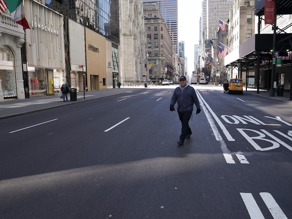 Un homme seul traverse la 5e Avenue à New York. Peu de passants et de véhicules sont présents aux alentours.