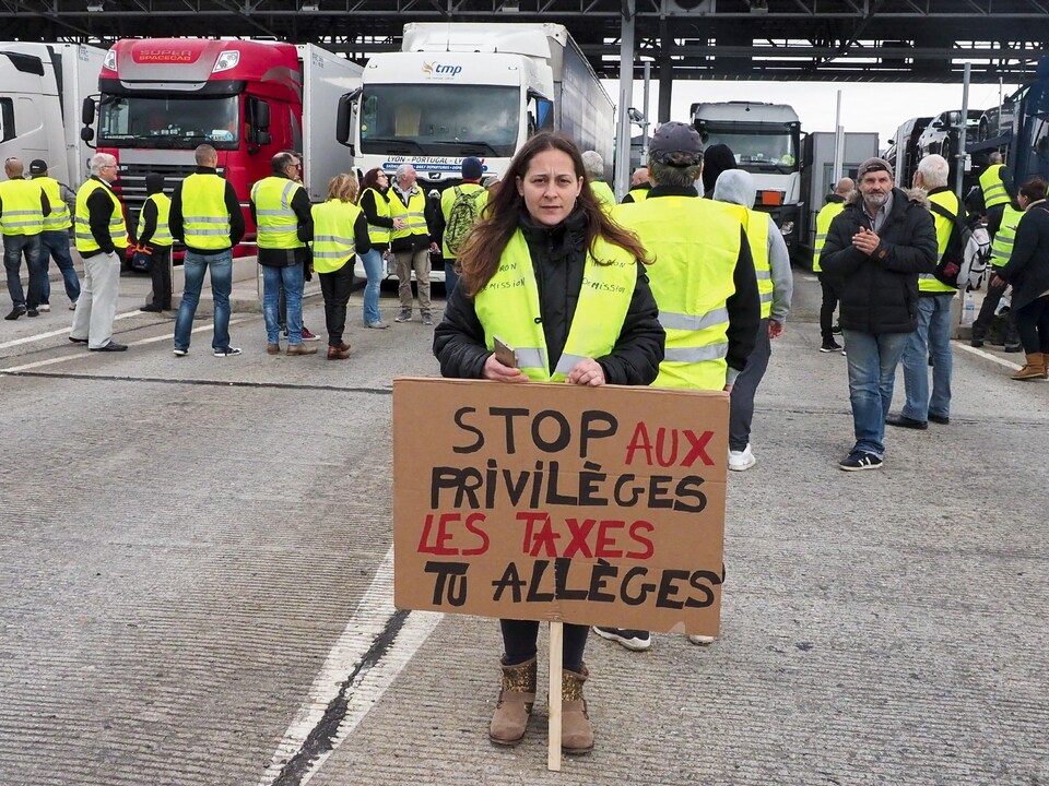 Une femme tient une pancarte où il est écrit : stop aux privilèges, les taxes tu allèges.