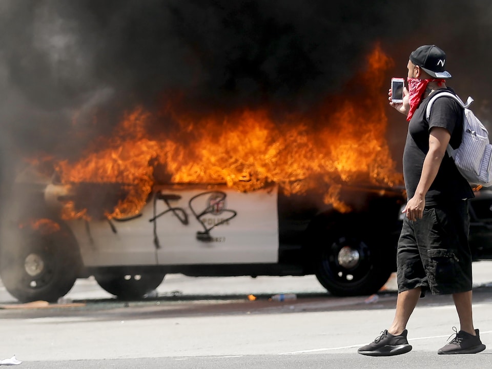 Un manifestant photographie une voiture de police incendiée.