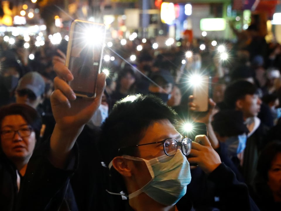 Des manifestants brandissent des cellulaires dont la lumière est allumée.