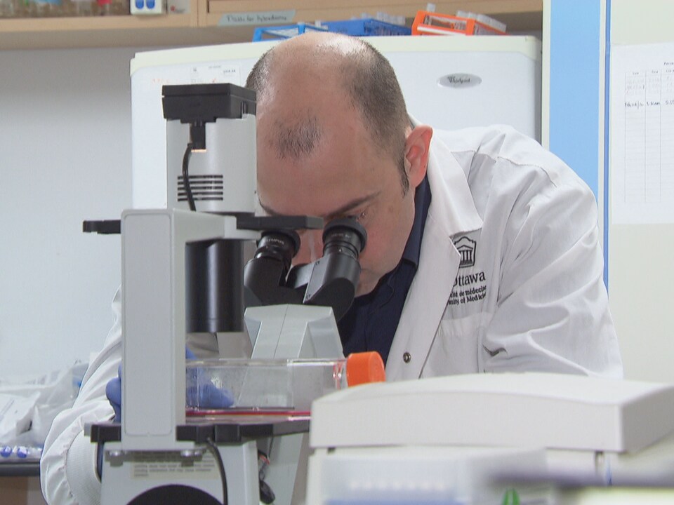 Marc-André Langlois regarde dans un microscope dans un laboratoire.