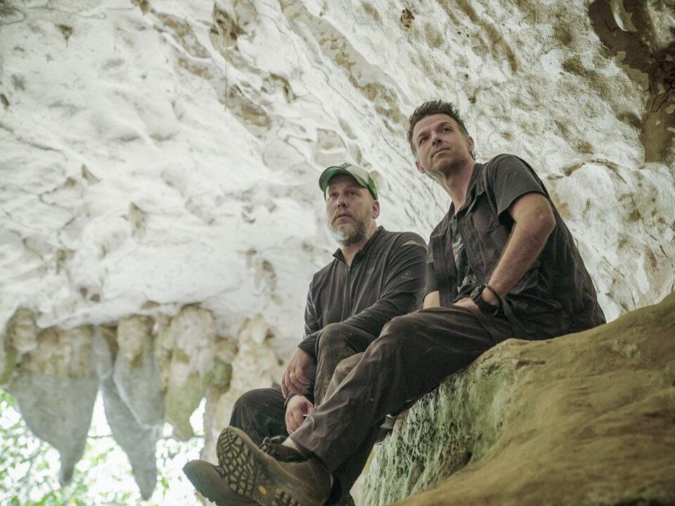 Deux hommes se tiennent sur un rocher dans une grotte.