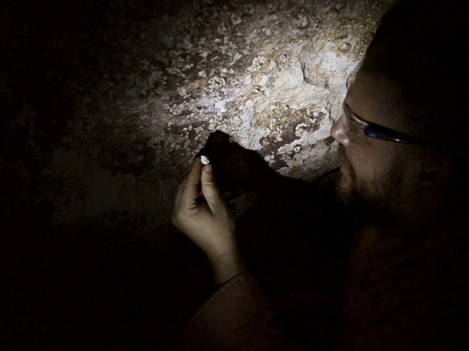 Maxime Aubert analyse des échantillons sur la paroi de la grotte.