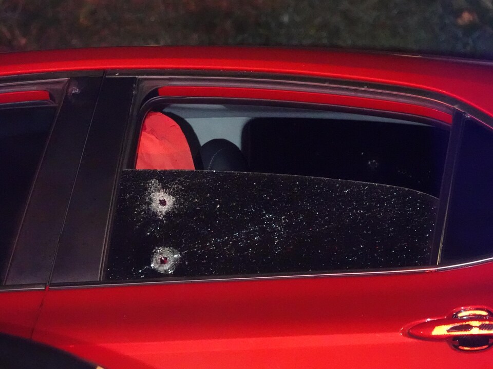 Deux impacts de projectiles d'arme à feu sont visibles sur la vitre arrière d'une voiture.