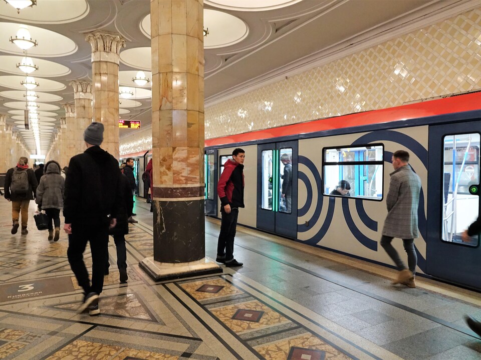 Des gens s'apprêtent à monter dans un train de la station Kievskaya, illuminée par une série de lustres sur le quai.