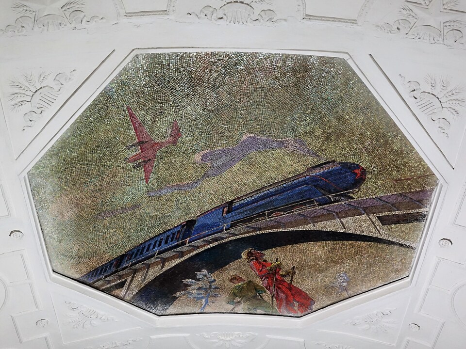 Sur cette mosaïque, un train à vapeur passe sur un viaduc, attirant l'attention de deux promeneurs en contrebas.
