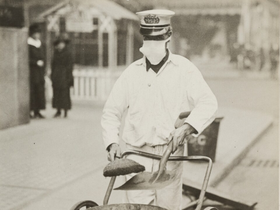 Une photo noir et blanc montre un nettoyeur de rue portant un masque.