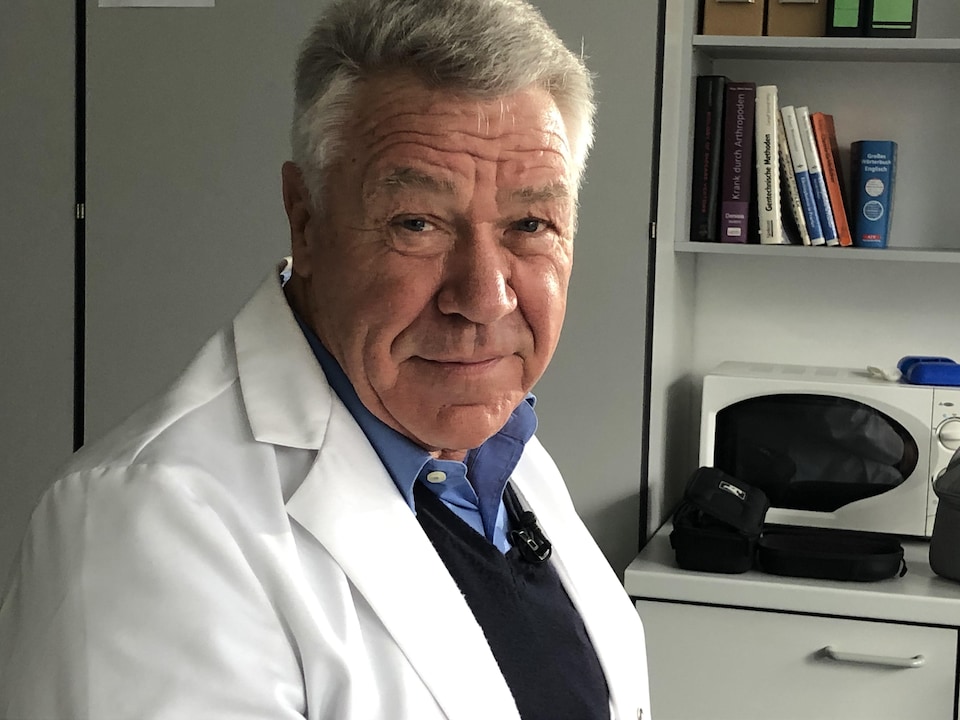 L'homme en sarrau sourit à l'objectif.