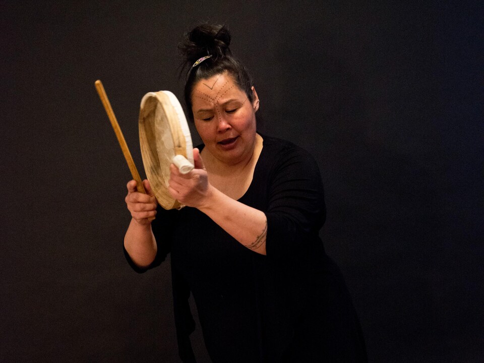 Une femme tient un tambour traditionnel du Groenland dans ses mains.