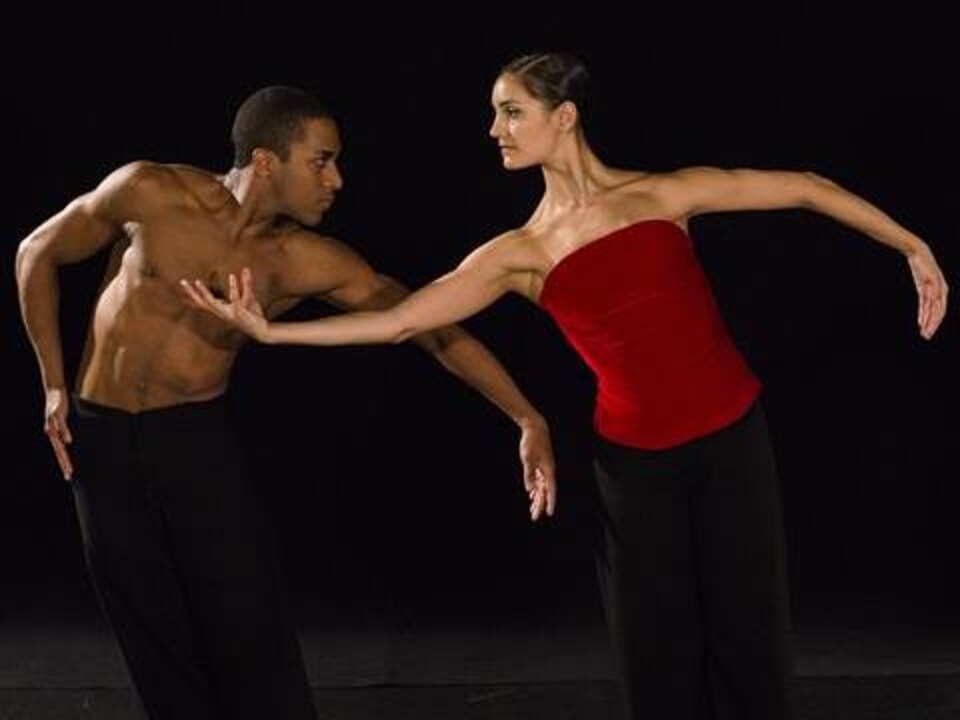 Two dancers, illuminated, on stage.