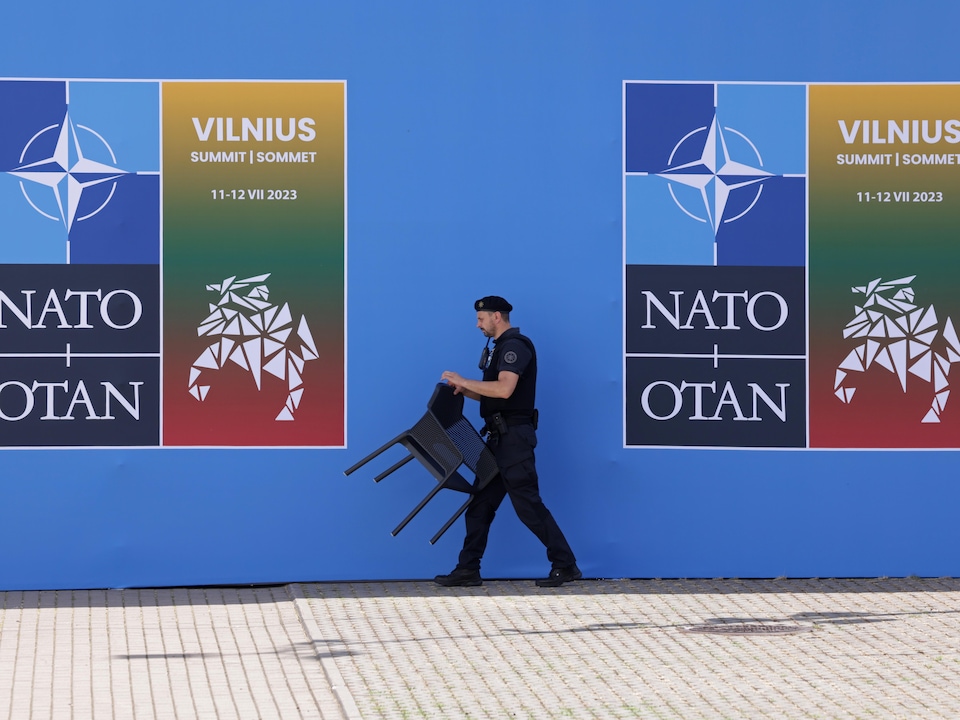 Um guarda de segurança move uma cadeira em frente às bandeiras da cúpula da OTAN.