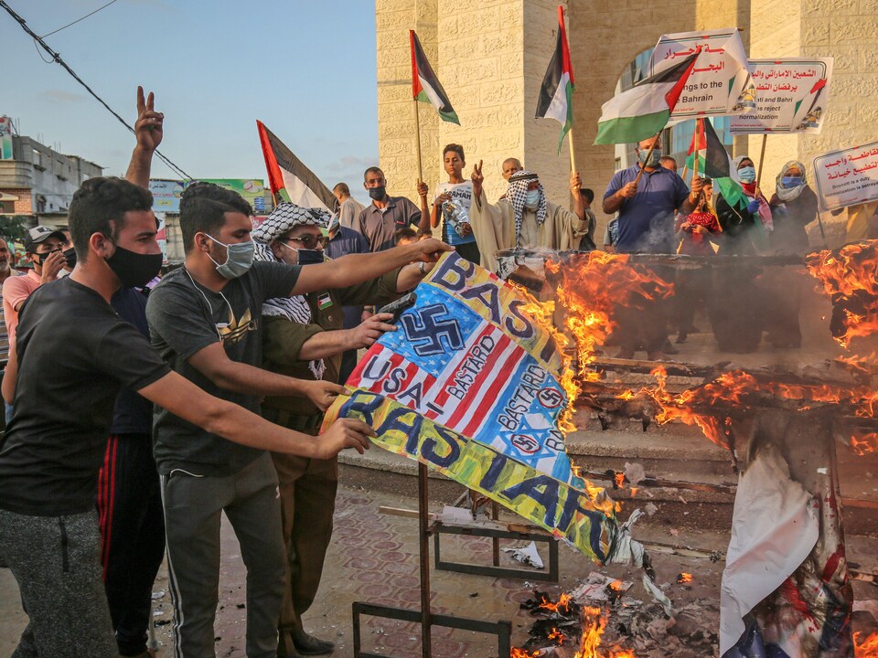 Des jeunes masqués brûlent des pancartes représentant le drapeau américain.