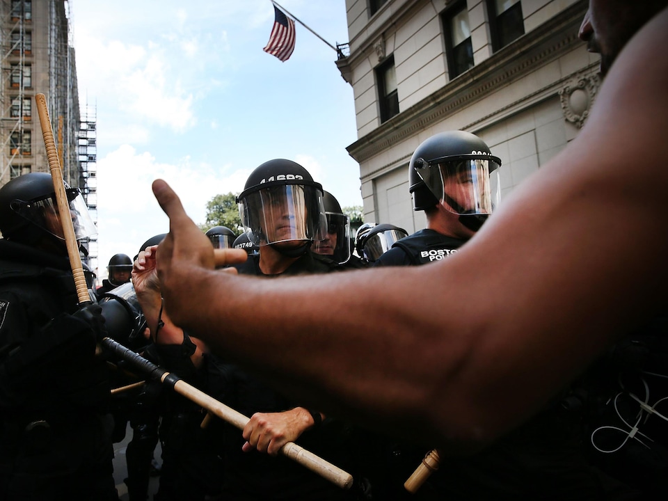 Boston police in riot gear face an African-American protester with only his arm visible.