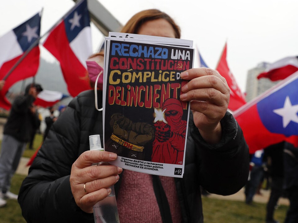 Une femme tient dans ses mains un tract sur lequel est écrit : « Je rejette une Constitution complice des délinquants ».