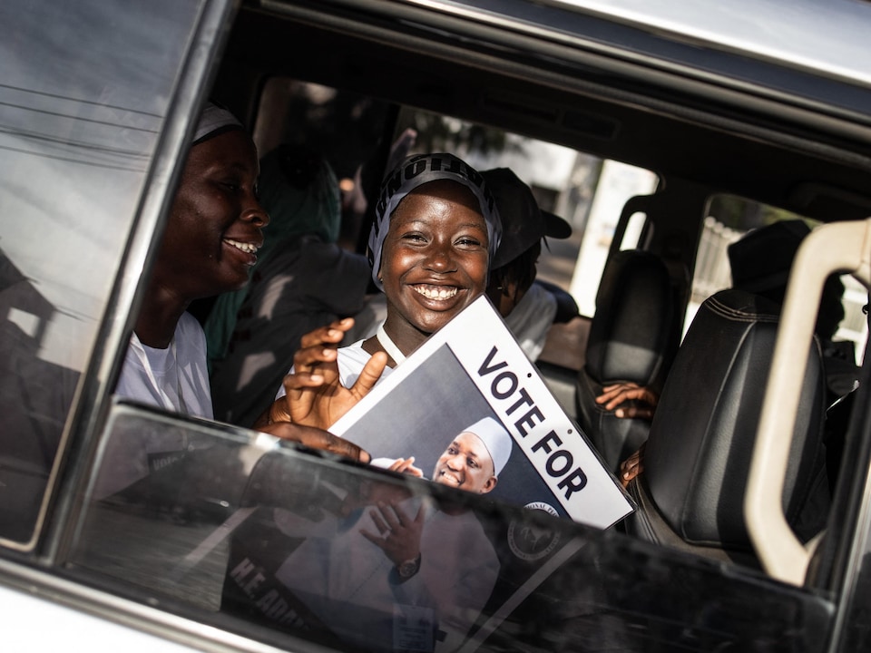 Des gens souriants tiennent une pancarte d'Adama Barrow.