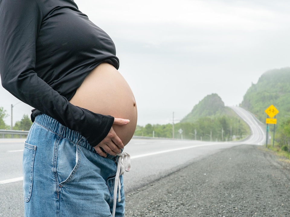 Une femme enceinte expose son ventre arrondi devant la route 132.