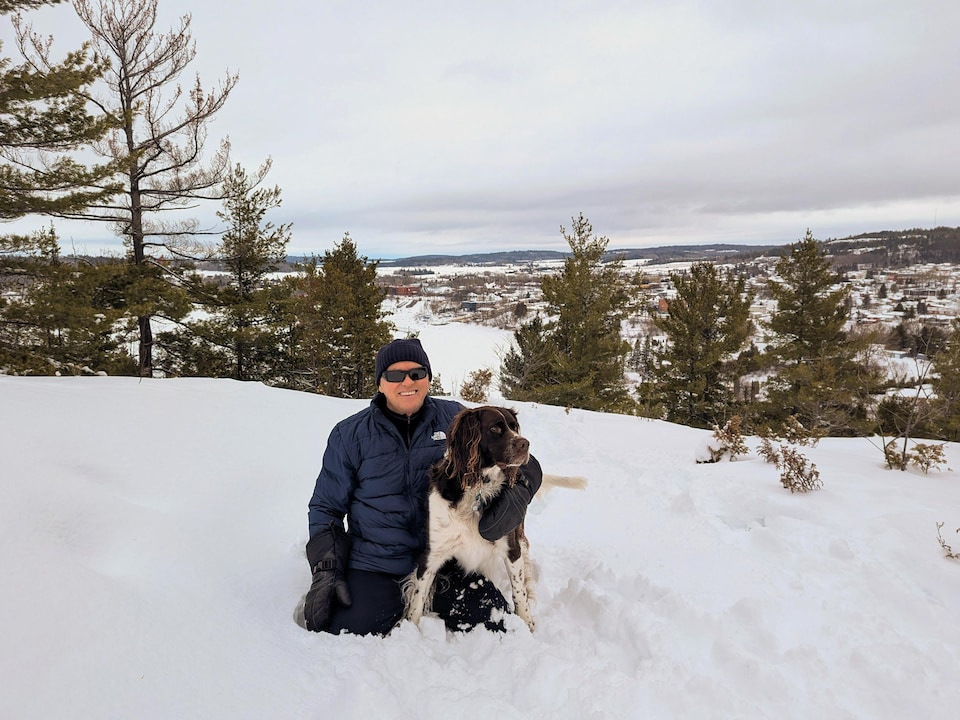 Gaston Saucier est à genoux dans la neige et entoure son chien avec son bras.