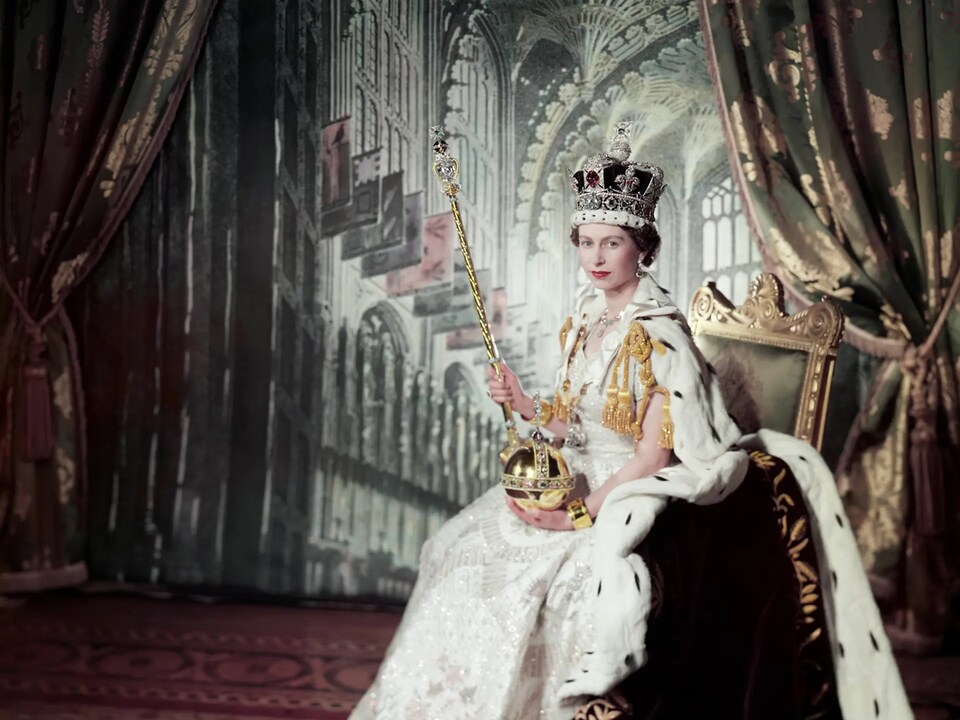 La reine Élisabeth II dans le palais de Buckingham, avec sa couronne. Elle est assise.
