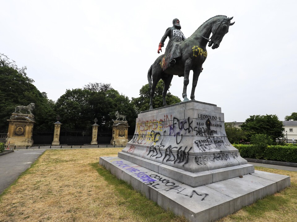 Léopold II assis sur un cheval monté sur un piédestal avec des mots comme «assassin» écrits dessus. 