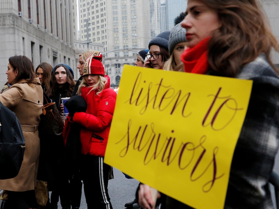 Des femmes sont rassemblées dans une rue de New York, l'une d'entre elles tient une affiche sur laquelle on peut lire : « Listen to survivors ».