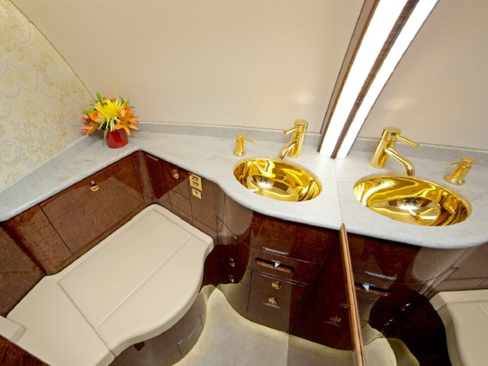 Le lavabo et le robinet de la salle d'eau de l'avion sont plaqués or. Les meubles semblent eux aussi en bois verni. Des fleurs ont été posées dans le coin de la cabine.