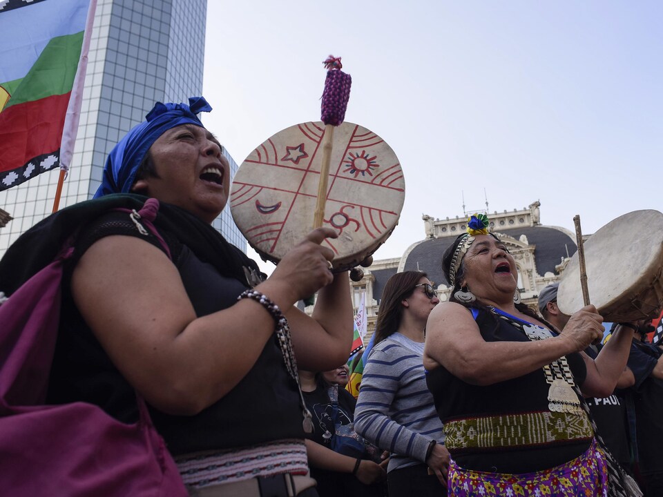 Deux femmes mapuches vêtues d'habits traditionnels jouent du tambour pendant une manifestation.