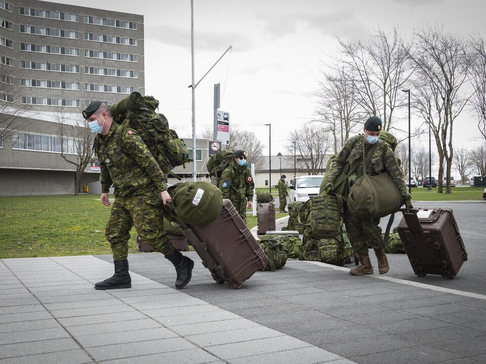 Un groupe de soldats en uniforme de combat, portant un masque chirurgical, arrivent au centre de formation avec leurs bagages.