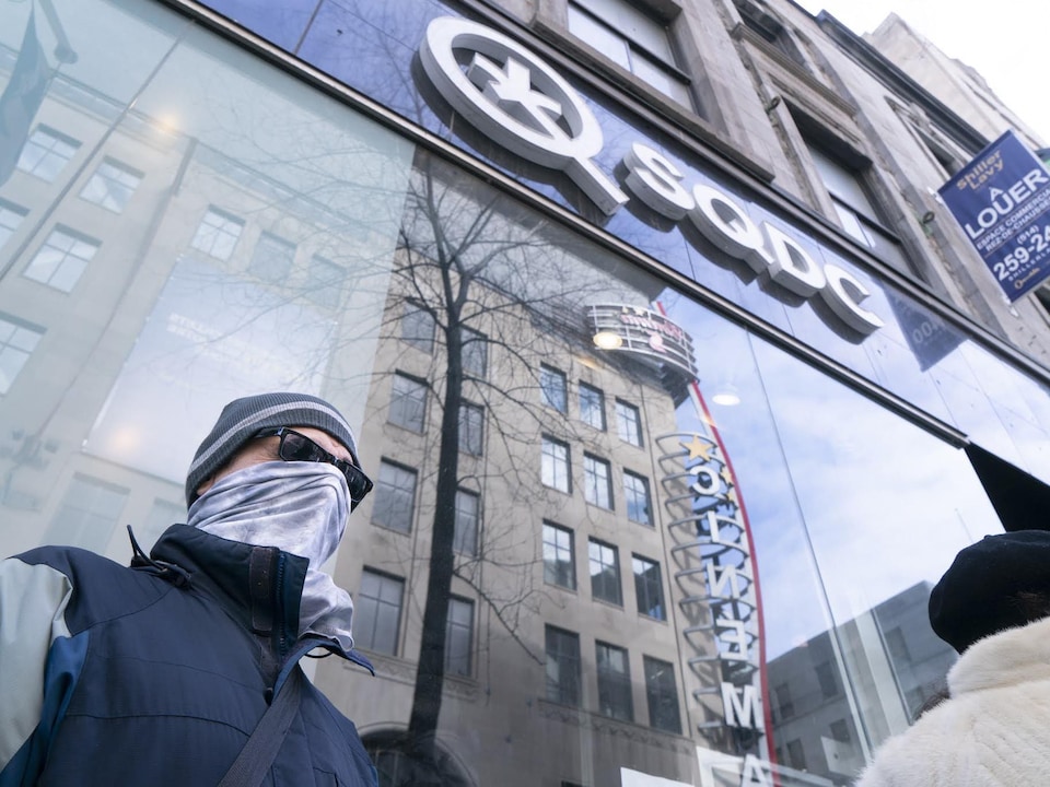 Un homme ayant remonté son chandail pour se cacher le visage attend devant une succursale de la Société québécoise du cannabis. 