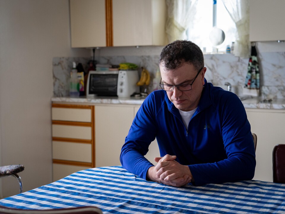 Sylvain Dufour est assis dans la cuisine de sa mère. Il regarde ses mains, qui sont croisées.