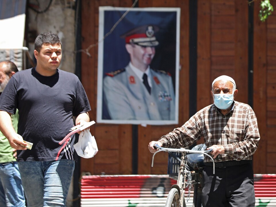 Un homme pousse son vélo tandis qu'un autre marche devant un portrait de Bachar Al-Assad.