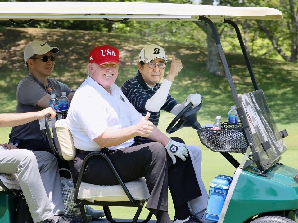 Deux hommes assis dans une voiturette de golf brandissent leur pouce en signe de bonne entente sur un terrain de golf.
