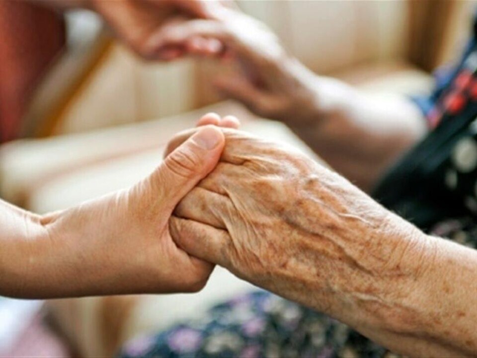 Gros plan sur les mains d'une préposée aux bénéficiaires qui tiennent celles d'une personne âgée.