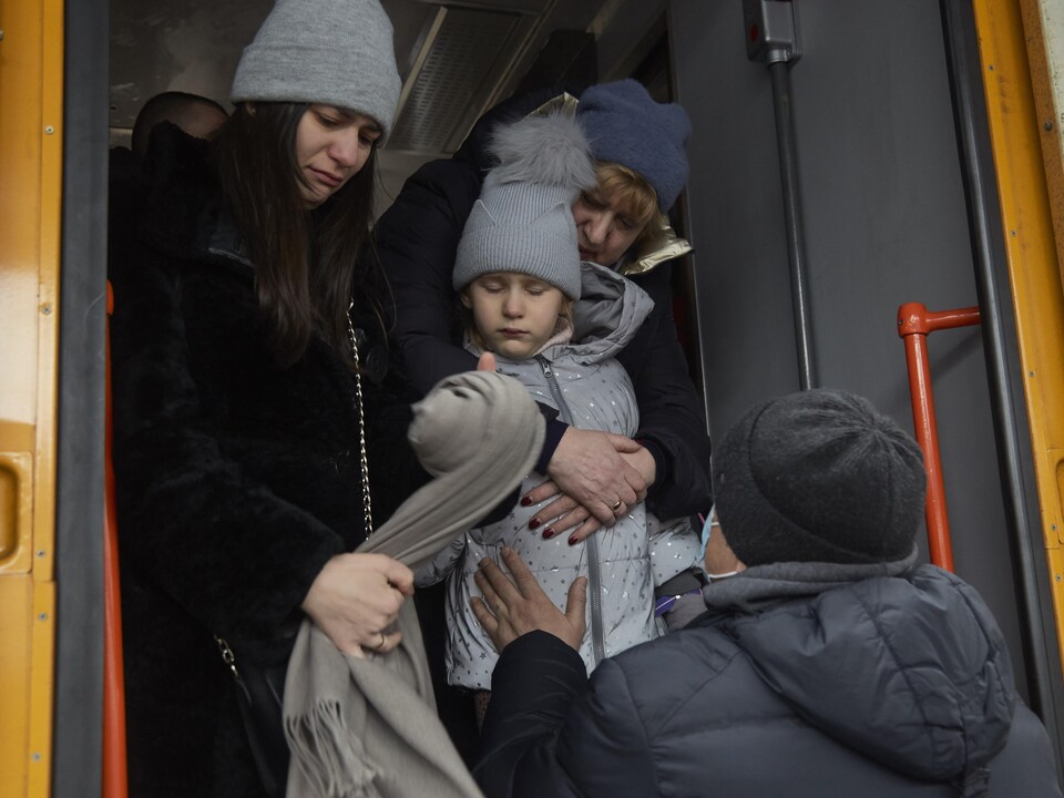 Un homme tient sa fille à la porte d'un train, sous les yeux tristes de sa femme.