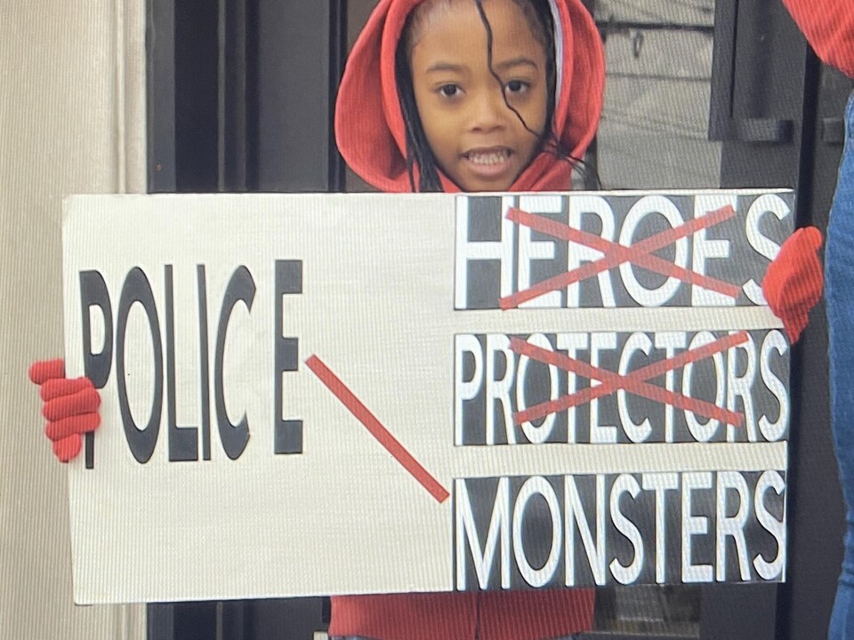Une petite fille tient une pancarte où il est inscrit que les policiers ne sont pas des héros qui protègent, mais des monstres